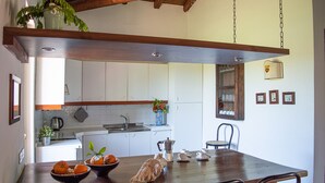 A kitchen with white cabinets, a wooden dining table, and a hanging light fixture. - Tenuta San Calogero (Augusta)