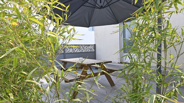 An outdoor patio with a wooden table and chairs under a black umbrella, surrounded by bamboo plants. - Quiet 2-bedroom house (Blanzy)