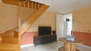 A staircase leading to a landing with a television on a wooden console table, a refrigerator, and a round wooden table with a basket. - Quiet 2-bedroom house (Blanzy)