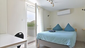 A bedroom with a bed, a table, and a chair. There is a window with curtains, an air conditioning unit on the wall, and a view of greenery outside. - Quiet 2-bedroom house (Blanzy)