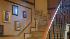 Una escalera con barandilla de madera y balaustres negros, que conduce a un rellano con cuadros enmarcados en la pared.