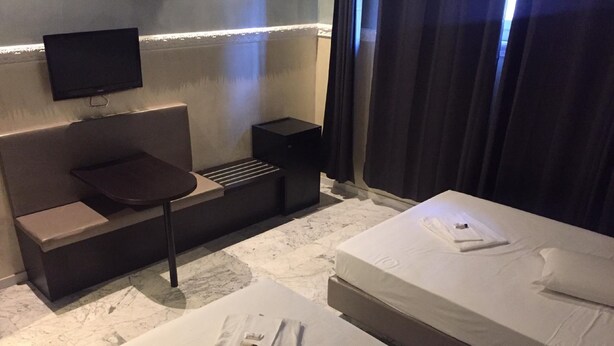 Habitación de hotel con sofá cama, una cama individual, un televisor montado en la pared y una mesita.