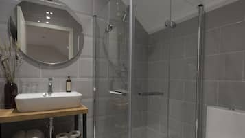 Un baño moderno con ducha de vidrio, un lavabo blanco y un inodoro.