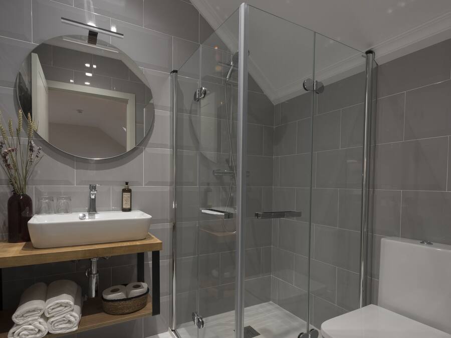 Un baño moderno con ducha de vidrio, un lavabo blanco y un inodoro.
