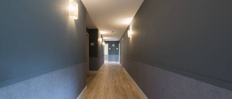 Un pasillo estrecho con suelo de madera y paredes grises, con luces empotradas en la pared y una puerta al final.