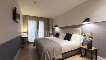 A modern bedroom with a large bed, bedside tables, a desk, and a wall-mounted TV.