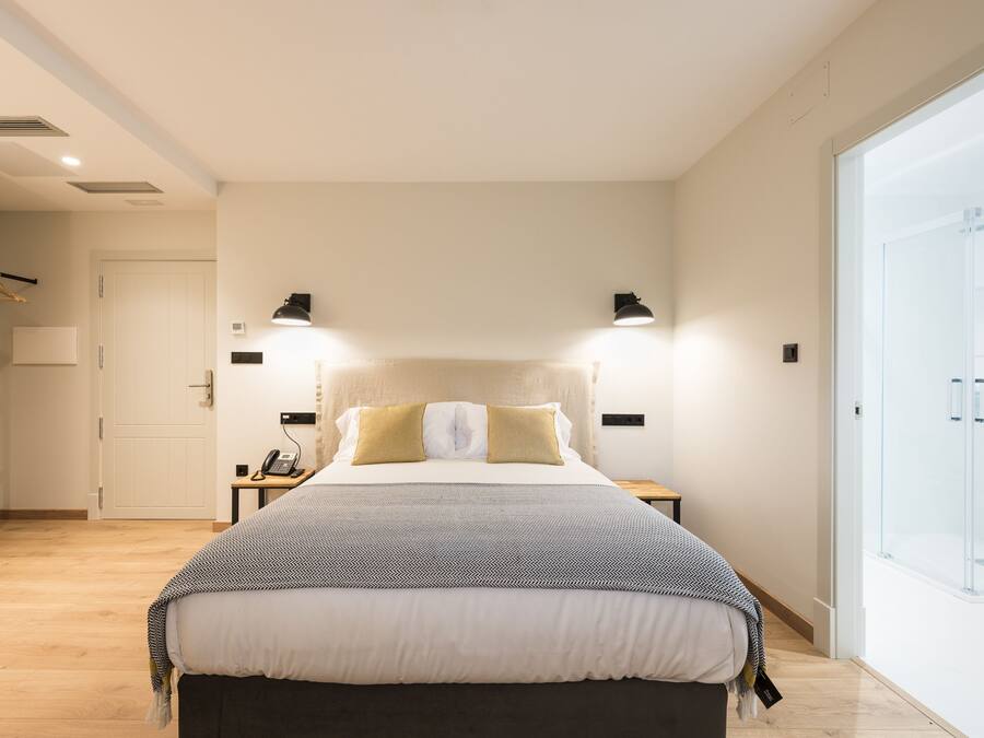 Ein modernes Schlafzimmer mit einem großen Bett, Nachttischlampen und einer Duschkabine aus Glas.