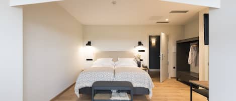 A bedroom with a bed, bedside lamps, a bench, and a desk.