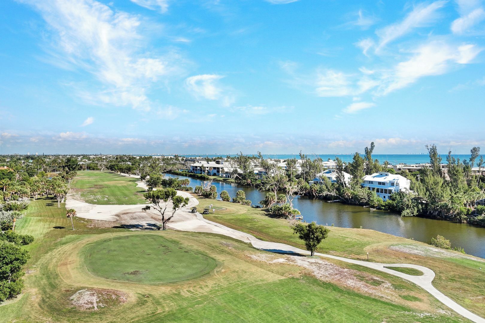 A golf course with a water body, trees, and buildings in the background.