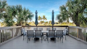 Una terraza de madera con una mesa y sillas, rodeada de palmeras y vista al agua.