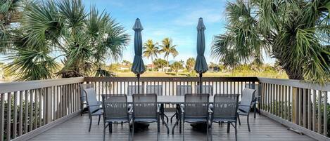 A wooden deck with a table and chairs, surrounded by palm trees and a view of the water.