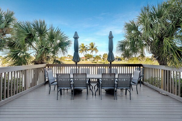 A wooden deck with a table and chairs, surrounded by palm trees and a view of the water.
