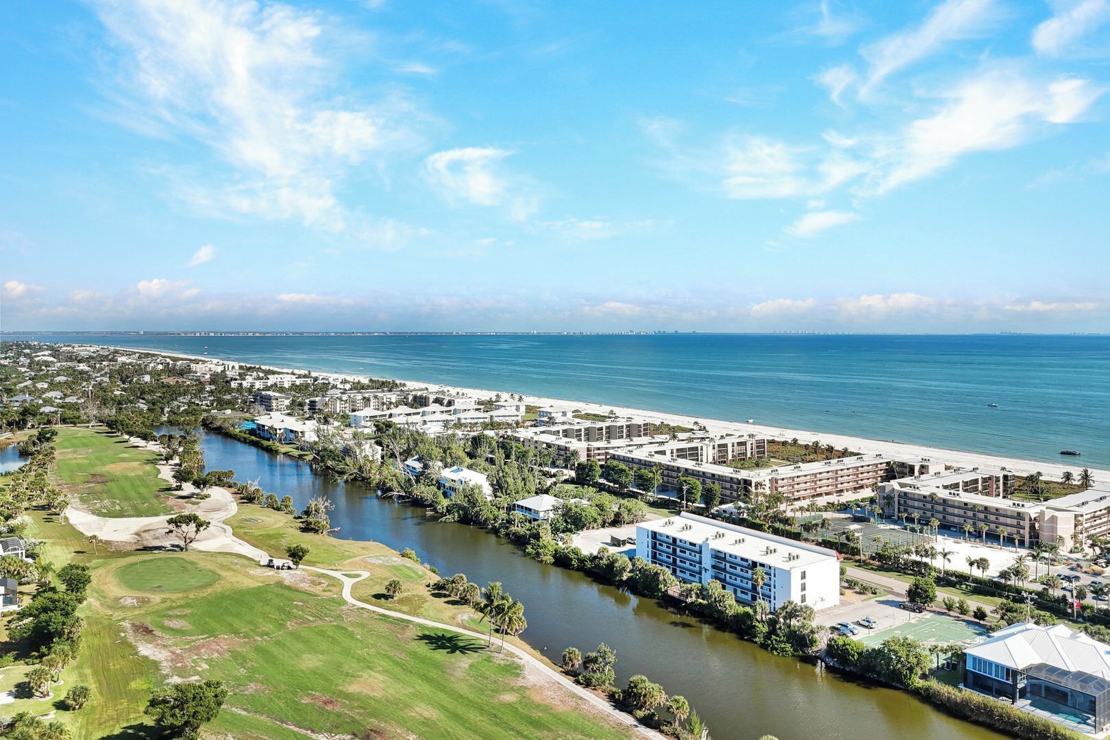 A coastal resort with a golf course, water body, and beachfront hotel buildings.