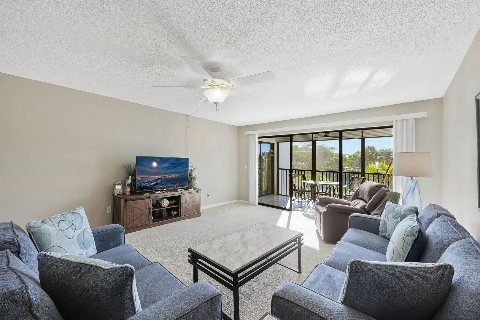 A living room with a TV, sofas, a coffee table, and a balcony with outdoor furniture.