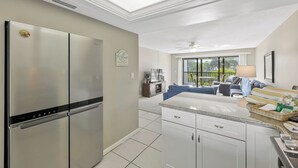 Una cocina moderna con un refrigerador de doble puerta, un comedor con mesa y sillas, y vistas al exterior a través de amplias ventanas.