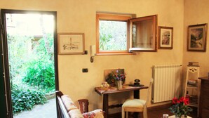 Ein gemütliches Zimmer mit einer Couch, einem kleinen Tisch mit einer Vase, einem Sessel und einem Fenster mit Blick auf Grünflächen.