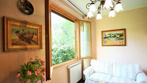 A room with a white striped sofa, a radiator, a window with a view of greenery, and two framed paintings on the wall. - Incenso Fine Studio in quiet Residence with Garden and Rooftop (Florence)