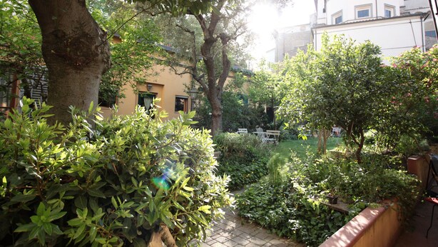 A garden with a paved path, a large tree, and a building in the background. - Incenso Fine Studio in quiet Residence with Garden and Rooftop (Florence)