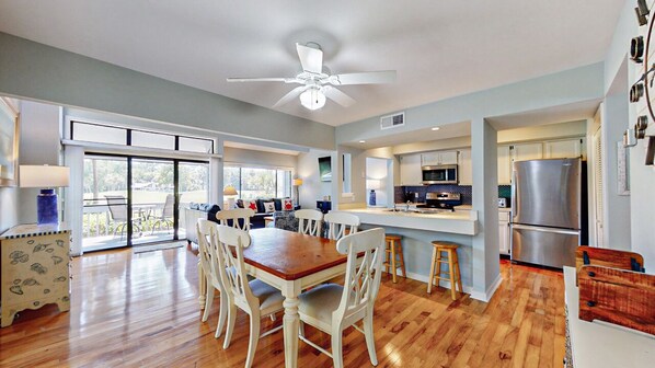 A spacious kitchen with a central island, a dining area with a wooden table and white chairs, and a large sliding glass door leading to a balcony.