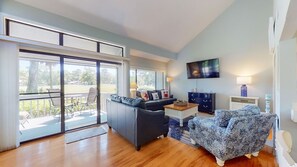 Ein geräumiges Wohnzimmer mit einem großen Schiebeglasfenster zum Patio, einem dunkelgrauen Sofa, einem gemusterten Sessel und einem kleinen Couchtisch.