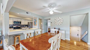 A modern kitchen with white cabinets, a wooden dining table, and a ceiling fan.
