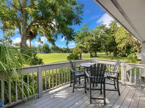 A wooden deck with a table and chairs, overlooking a well-maintained lawn and trees.