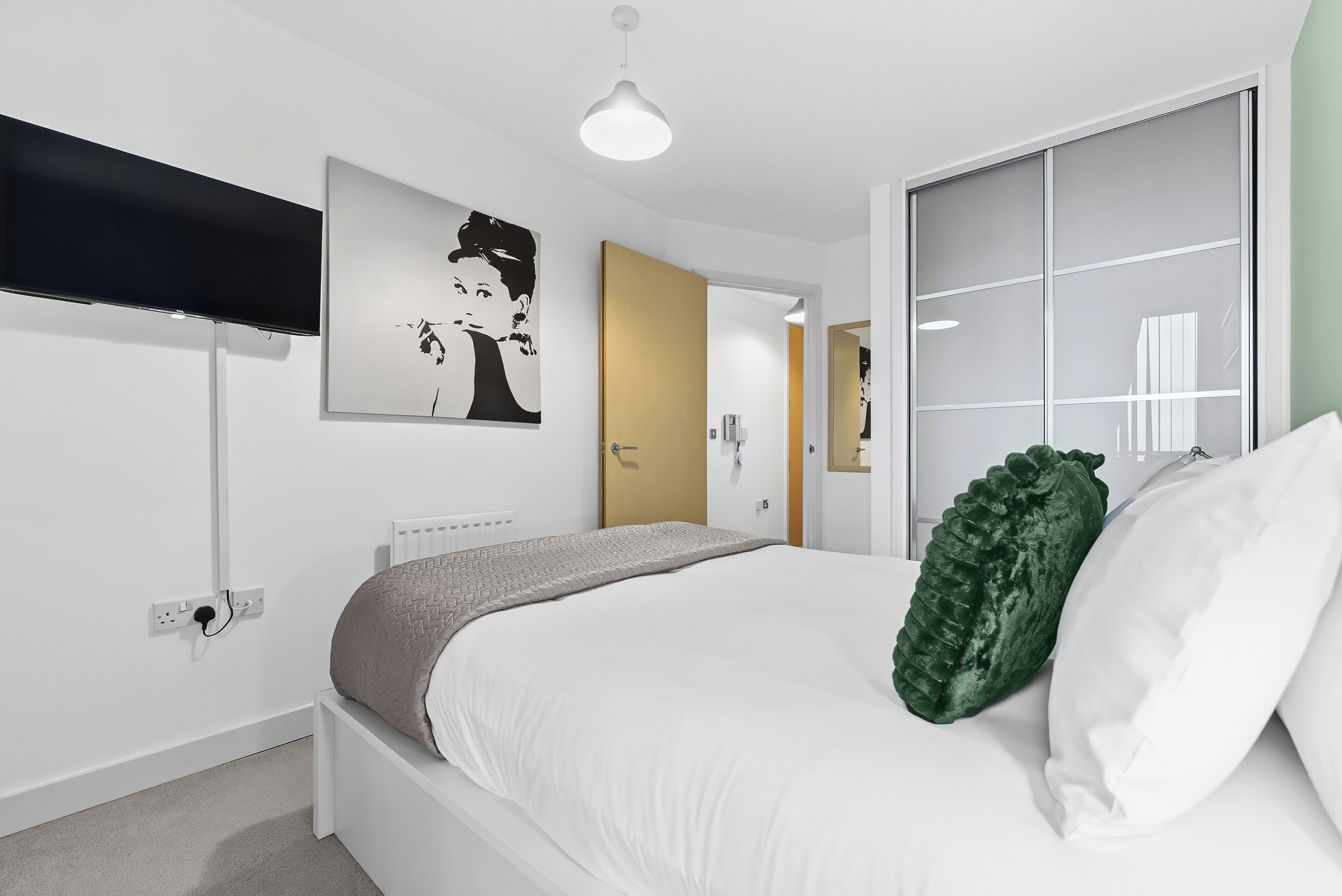 A modern bedroom with a bed, a flat-screen TV, a painting, and a sliding door.