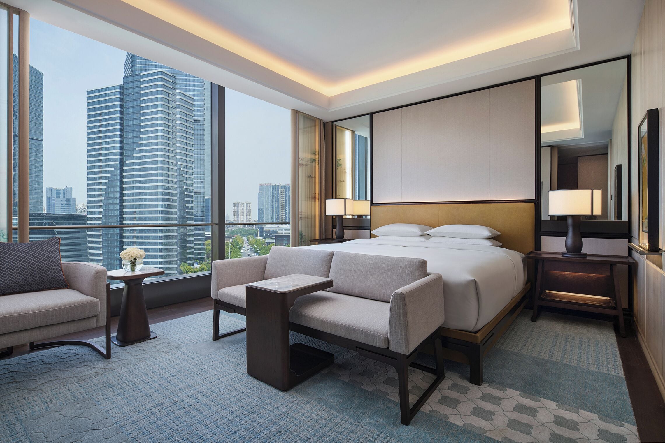 A modern hotel room with a large bed, two bedside tables, a sofa, and a chair.
