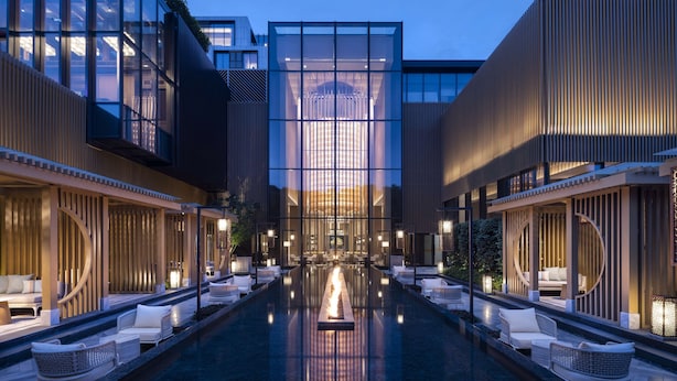 Un hotel moderno con piscina central, áreas de descanso con asientos y fachada de vidrio.
