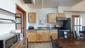 A kitchen with wooden cabinets, a stainless steel refrigerator, a microwave, and a dining table with chairs. - Large Groups | WiFi | Wheeler Peak Lodge (Angel Fire)