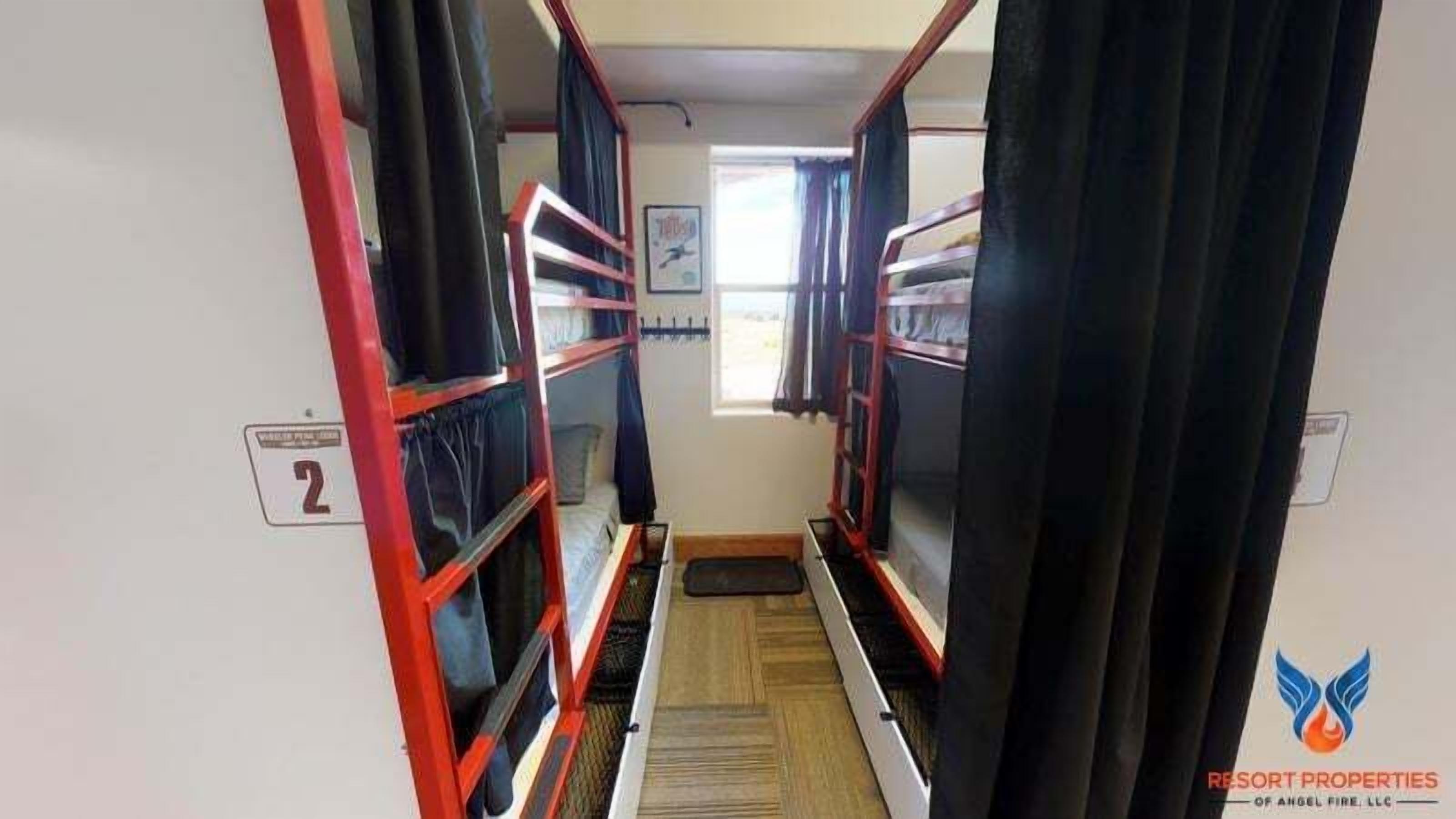 Un couloir étroit avec des lits superposés, une fenêtre avec des rideaux et une porte au fond.