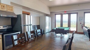 A kitchen with a stove, refrigerator, and dining area with chairs and a pool table. - Large Groups | WiFi | Wheeler Peak Lodge (Angel Fire)