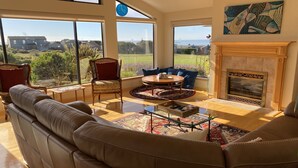 A spacious living room with a leather sofa, a round coffee table, and a fireplace. Large windows offer a view of the outdoors. - Ocean, Golf course and Mountain Views.Walk 3/4mi to the beach (Bodega Bay)