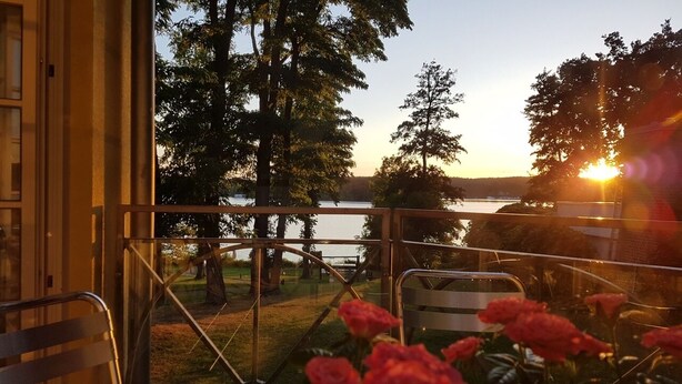 A balcony with a view of a lake and trees during sunset.
