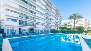 A hotel with a large swimming pool, multiple balconies, and a clear view of palm trees. - NEW Apt RELAX HOME 150 meters from the beach, WIFI and Pool (Port d'Alcúdia)