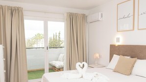 A hotel room with a bed, a chair, a balcony, and a view of trees. - NEW Apt RELAX HOME 150 meters from the beach, WIFI and Pool (Port d'Alcúdia)