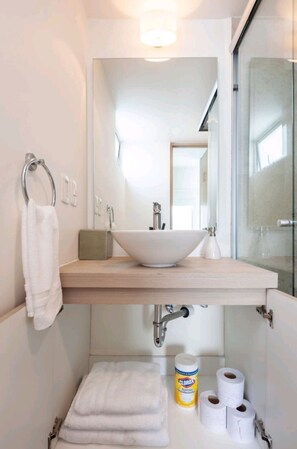 Ein Badezimmer mit weißem Waschbecken, einem Spiegel, einem Handtuchhalter und einer Duschkabine aus Glas.