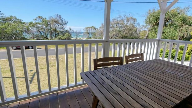 A wooden deck with a table and chairs, overlooking a road and greenery. - Abbey Beachviews with WiFi (Abbey)