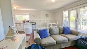 A living room with a beige sofa, a coffee table, and a dining area with a white table and chairs. - Abbey Beachviews with WiFi (Abbey)