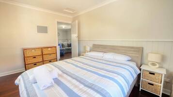 Une chambre à coucher comprenant un lit, des tables de chevet, une commode et une porte donnant sur une autre pièce.