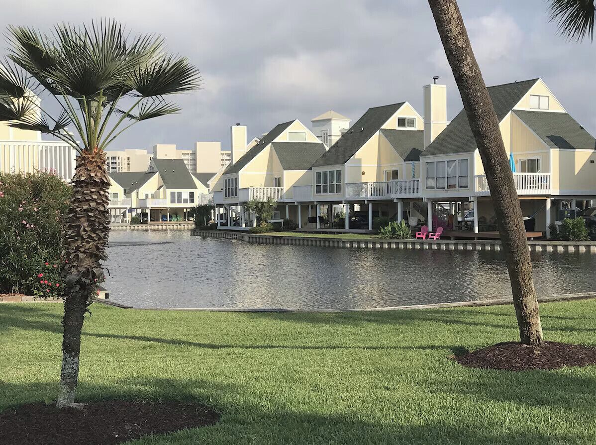A waterfront hotel with multiple balconies, a pool, and a palm tree.