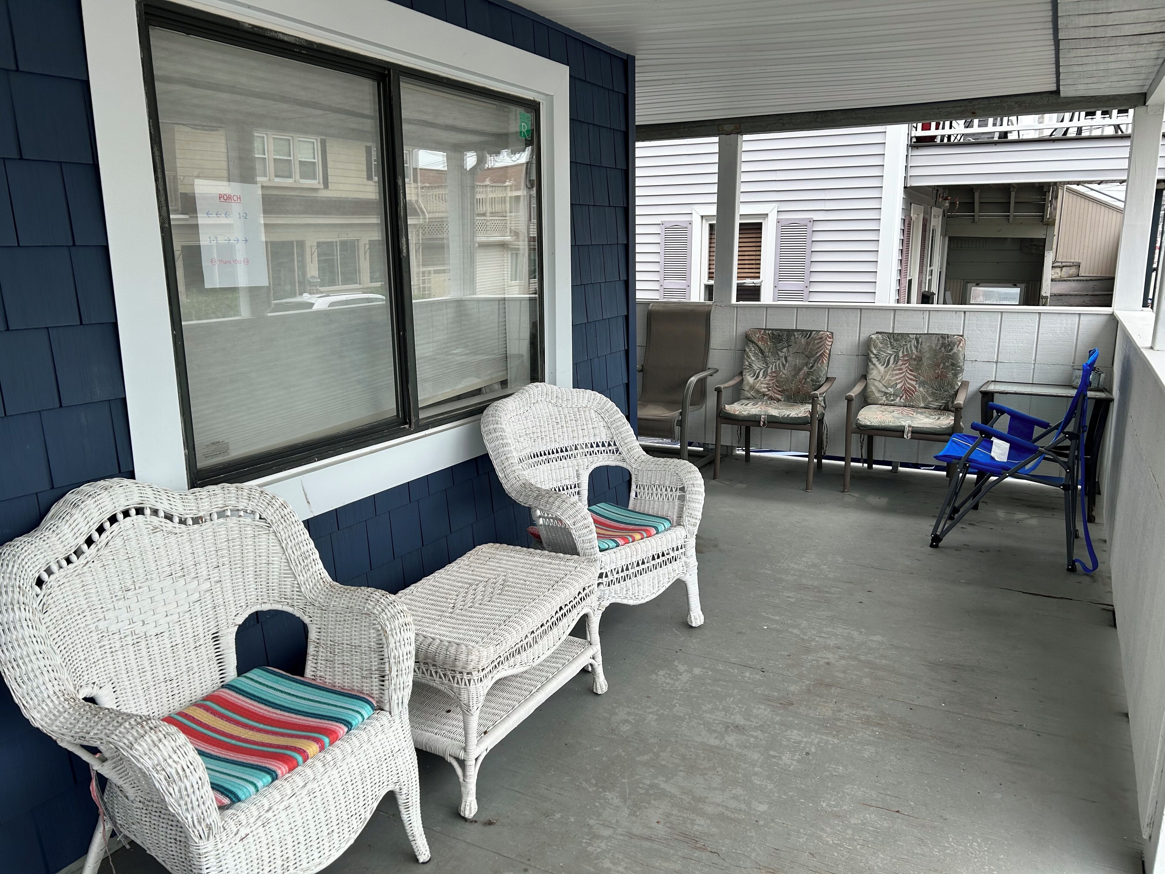 A covered outdoor seating area with wicker chairs and a blue folding chair.