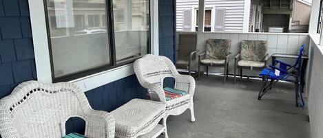 A covered outdoor seating area with wicker chairs and a blue folding chair.