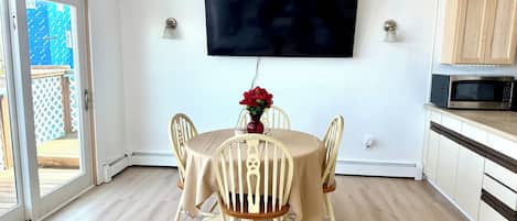 Un espace repas comprenant une table, des chaises, un téléviseur à écran plat et une cuisine équipée d’armoires et d’un four à micro-ondes.