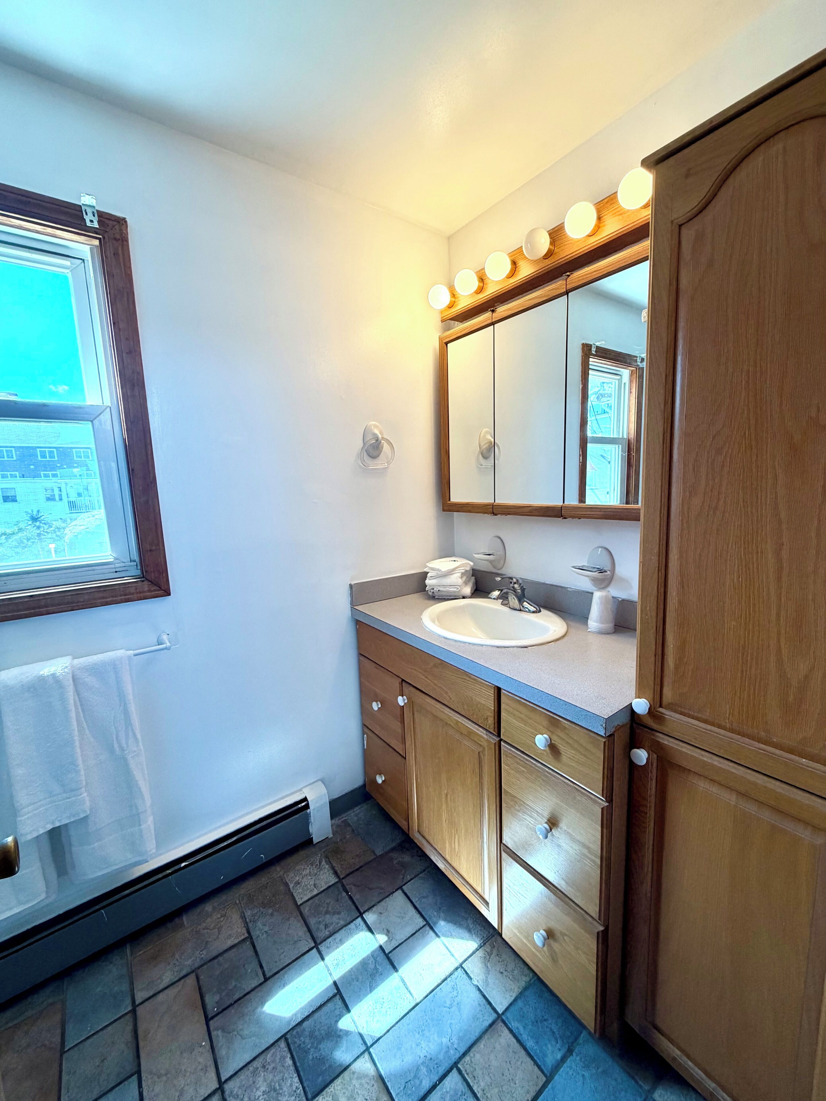 A bathroom with a sink, mirror, wooden cabinets, and a window with blinds.