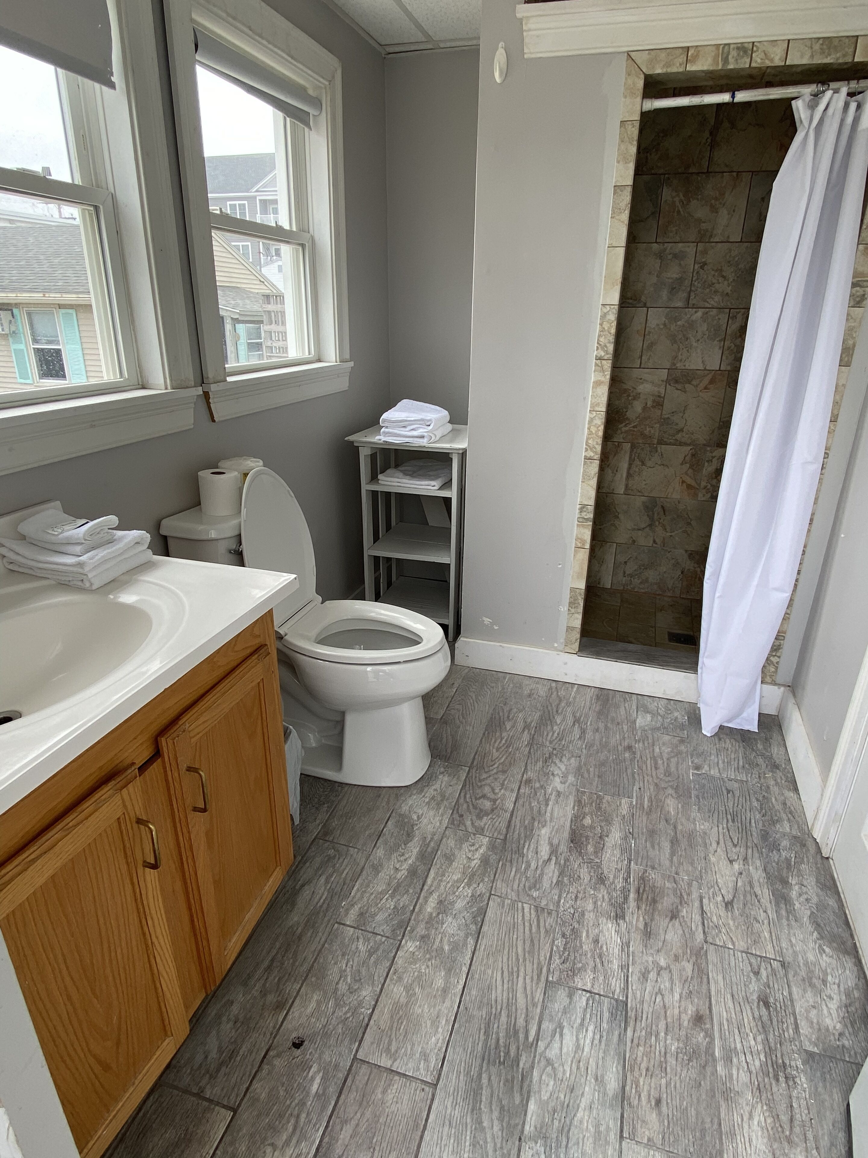 Un baño con tocador de madera, inodoro, ducha con cortina y ventana.