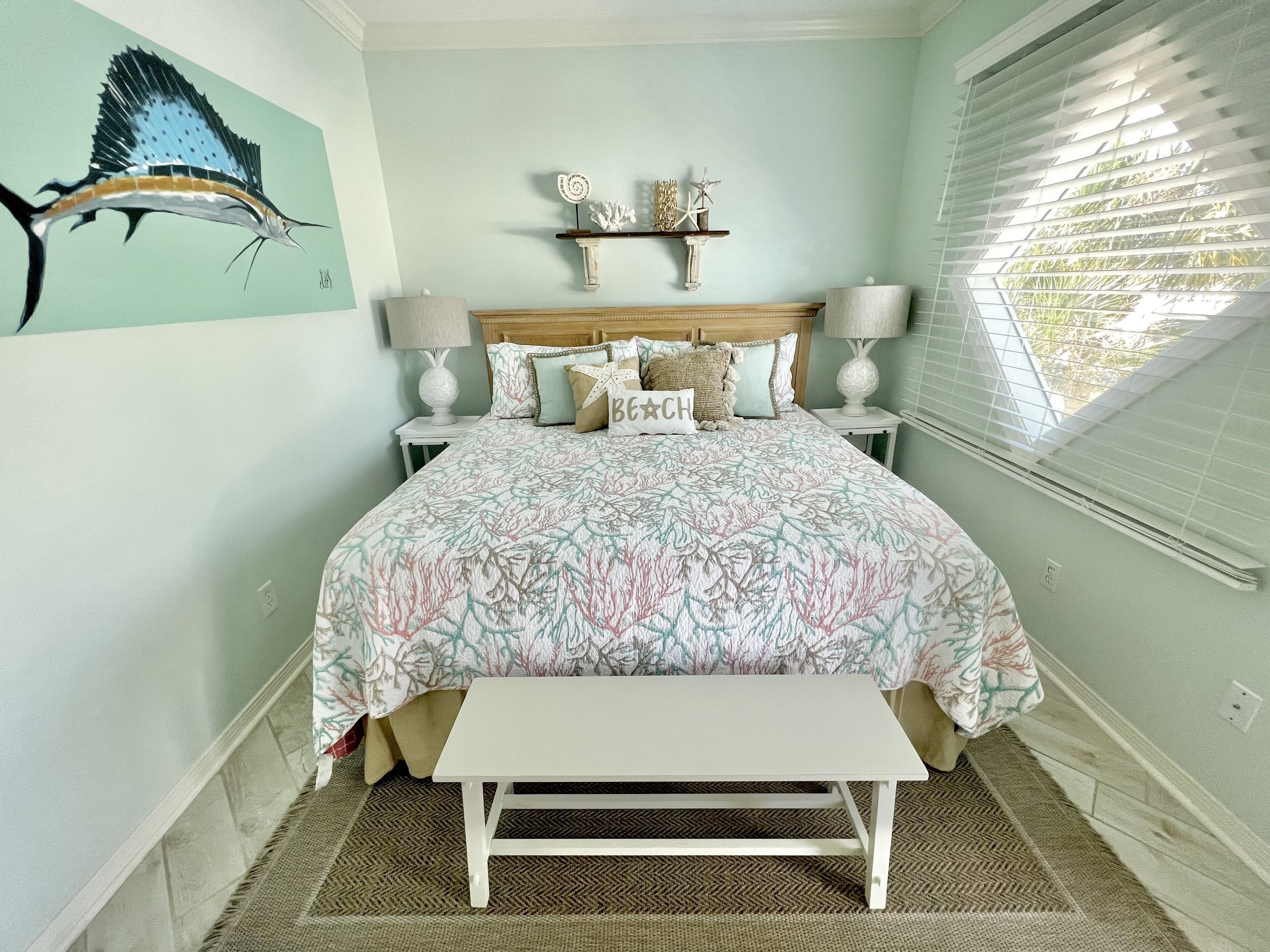 A bedroom with a bed, bedside tables, a bench, a wall with a painting, and a window with blinds.