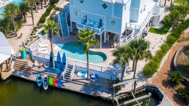 Un grand bâtiment de couleur bleu clair, doté d’une piscine, entouré de palmiers et comprenant un quai avec des kayaks.