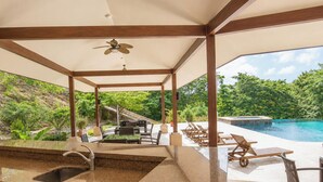 A covered outdoor area with a pool, lounge chairs, and a grill.