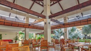 A spacious indoor area with multiple wooden tables and chairs, large windows, and a ceiling with exposed beams.